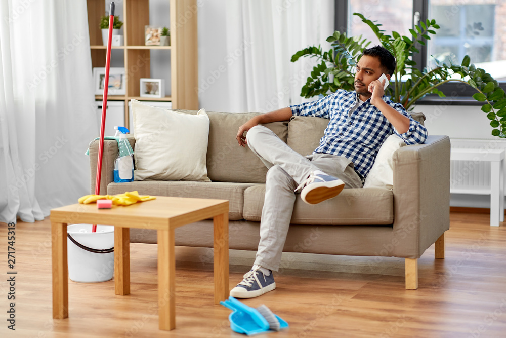 household and technology concept - indian man calling on smartphone after cleaning home household and technology concept - indian man calling on smartphone after cleaning home
