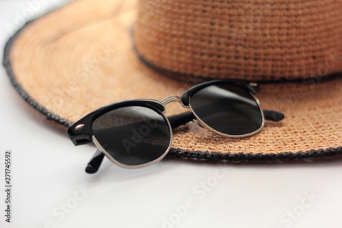 Closeup of black sunglasses and a straw hat on a white background. 