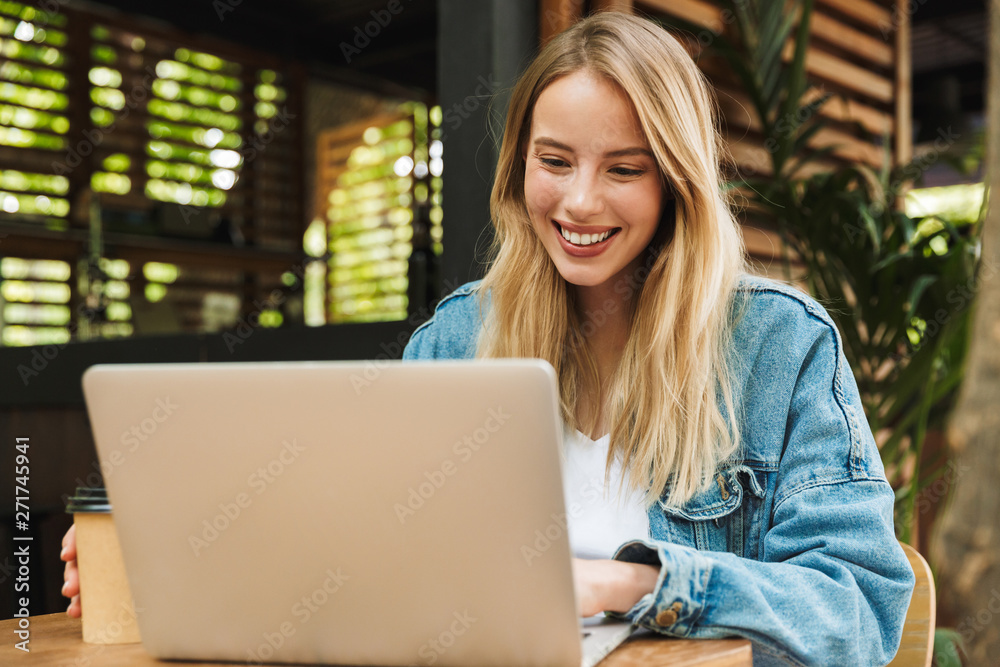 Amazing happy young woman posing outdoors in cafe using laptop computer. Amazing happy young woman posing outdoors in cafe using laptop computer.