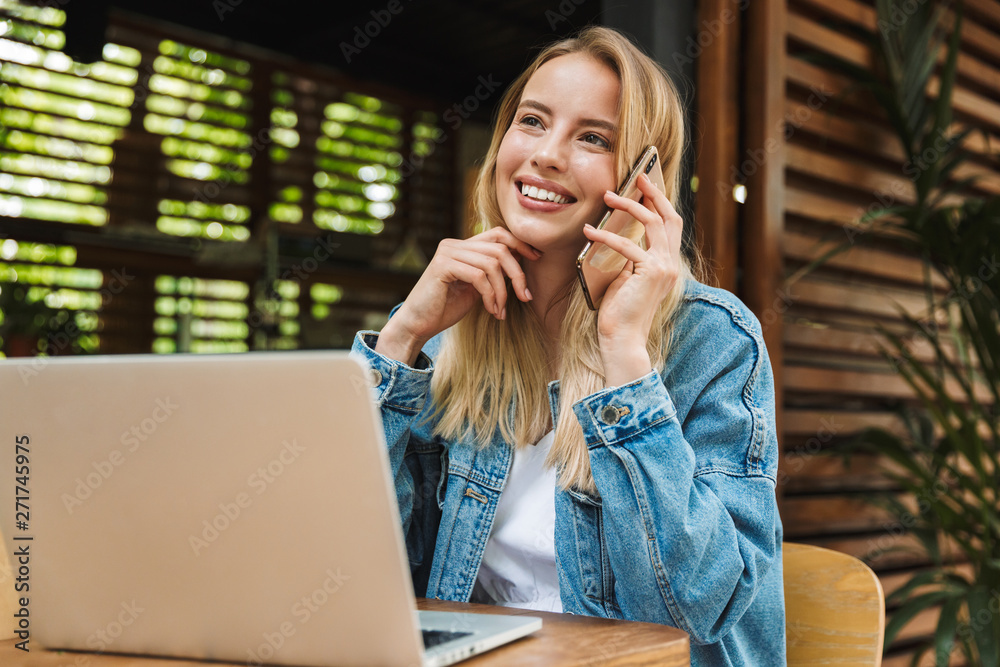 Excited happy young woman posing outdoors in cafe using laptop computer and talking by mobile phone. Excited happy young woman posing outdoors in cafe using laptop computer and talking by mobile phone.