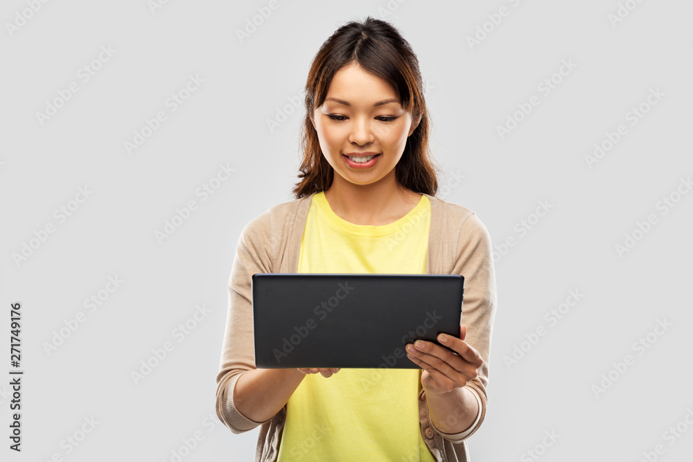 technology and people concept - happy asian woman using tablet computer over grey background technology and people concept - happy asian woman using tablet computer over grey background