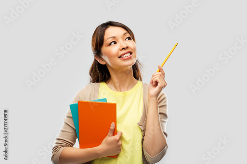 education, high school and knowledge concept - asian student woman with books and pencil over grey background