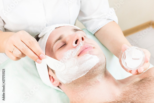 A young man is undergoing a mask treatment in a beauty salon spa. 