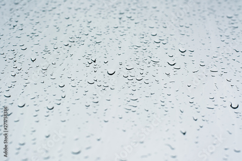 Rain drops on a window glass surface against a white background of rainy clouds.