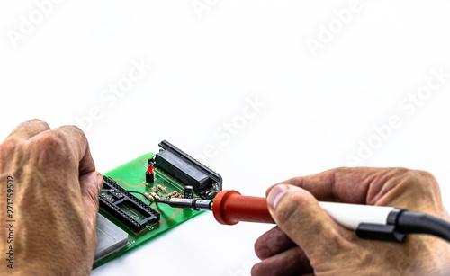 Male hands solder components onto a printed circuit board using tin and a soldering iron