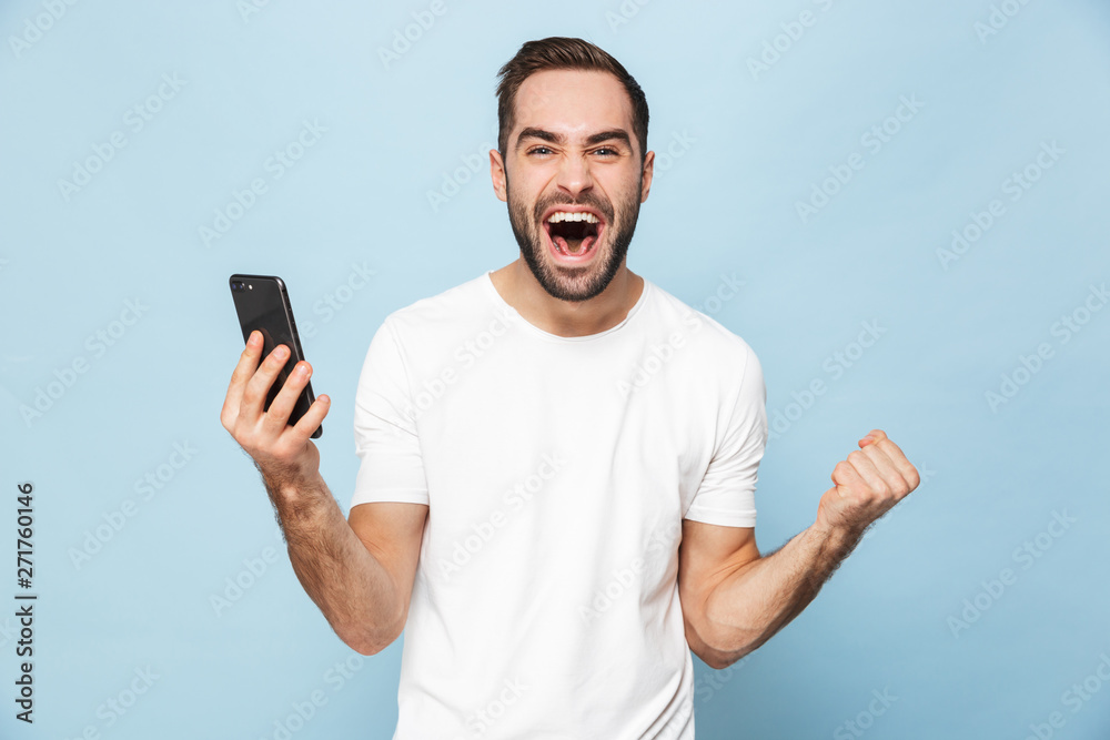Handsome excited young man using mobile phone isolated over blue wall background. Handsome excited young man using mobile phone isolated over blue wall background.