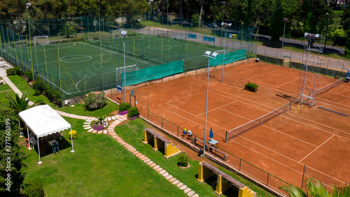 Aerial view perpendicular to two soccer fields at 5 and a red ground tennis court. On board camp benches and umbrellas. The fields are empty because it is summer and hot.