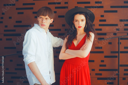 Beautiful fashionable couple on an abstract background. Fashionable hipsters. Girl in a red dress and black big hat. A man with glasses and a white shirt. Model pouse. photo