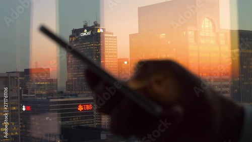 NEW YORK, UNITED STATES OF AMERICA, DECEMBER 2017: CLOSE UP DOF: Scenic shot of corporate skyscrapers illuminated by burnt orange sunset as the woman writes a text message from her office in New York. photo
