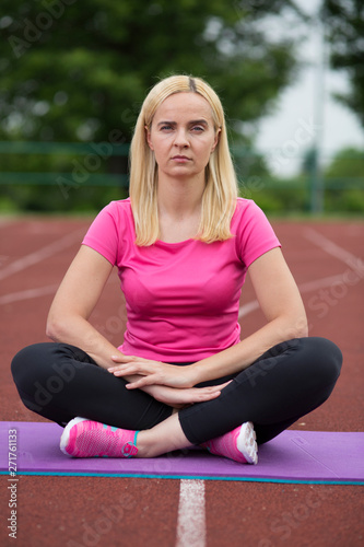 Fit girl practicing stretching exercise at stadium.A girl is training on a sports field. Young beautiful girl in sports uniform posing on sports field. Fitness blonde girl doing exercises in the fresh