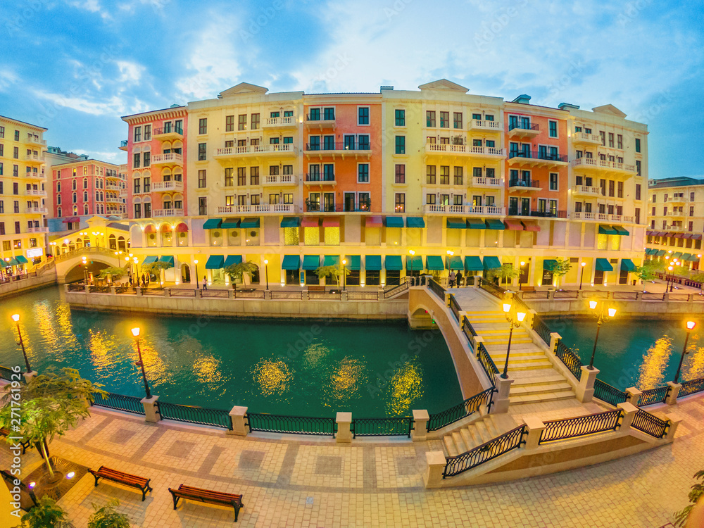 Wide angle view of two Venetian bridges on canals of picturesque district icon of Doha illuminated at night. Panorama of Venice at Qanat Quartier, the Pearl-Qatar, Middle East. Twilight shot.