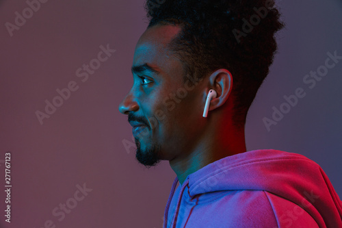 Portrait in profile of positive african american man in colorful hoodie listening to music with earpod photo