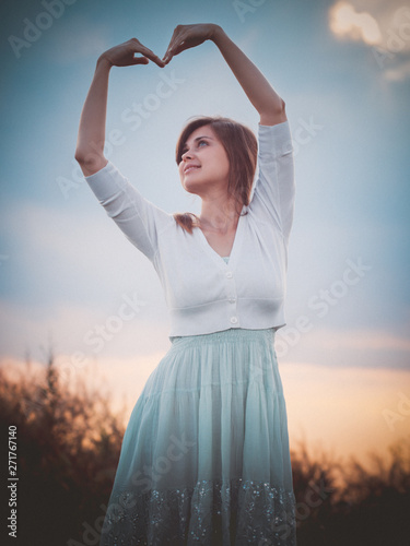 beautiful girl in the field folded her hands in the shape of a heart, a young girl walking, the concept of beauty, nature, youth, love and feelings photo