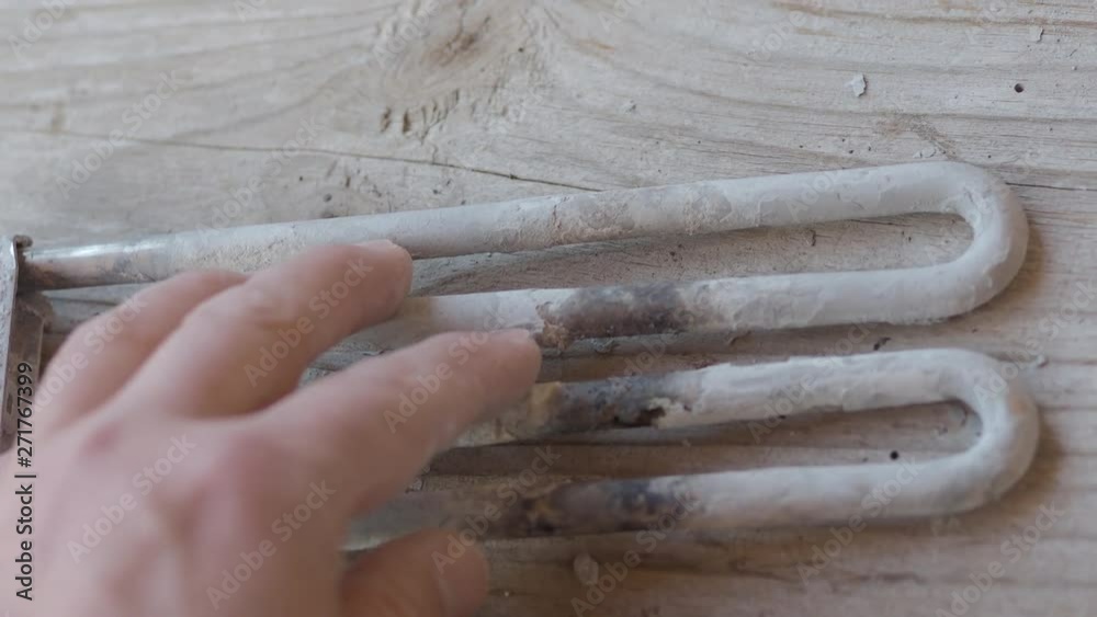 Burnt-out heating element from a washing machine. Man is touching turbular electric heating element covered with limescale. Burnt-out heating element from a washing machine. Man is touching turbular electric heating element covered with limescale.