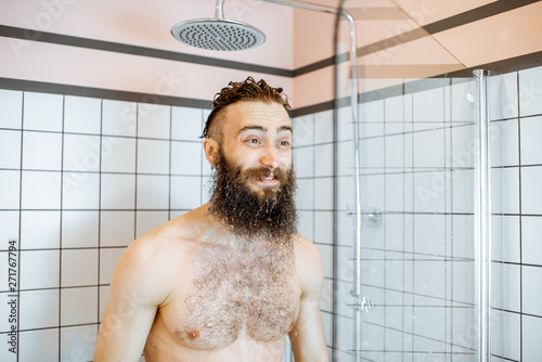 Bearded man feeling shocked while taking a shower with cold water in the bathroom at home