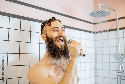 Joyful bearded man singing into the micrphone while taking a shower in the bathroom photo