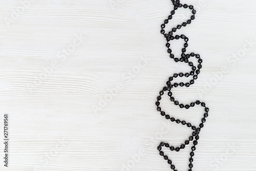 String of black beads on white wood background. Frame from Black stone beads. Necklace closeup. Copy space. Top view. photo