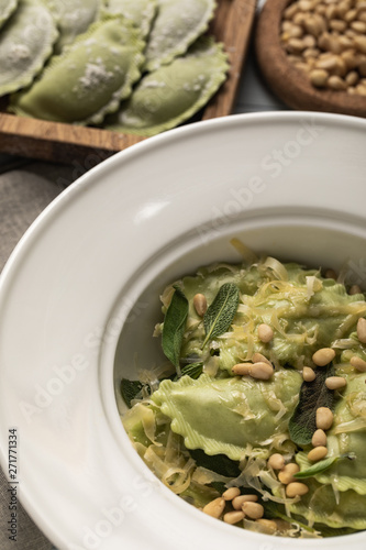 close up view of tasty green ravioli served in plate with sage, pine nuts and grated cheese