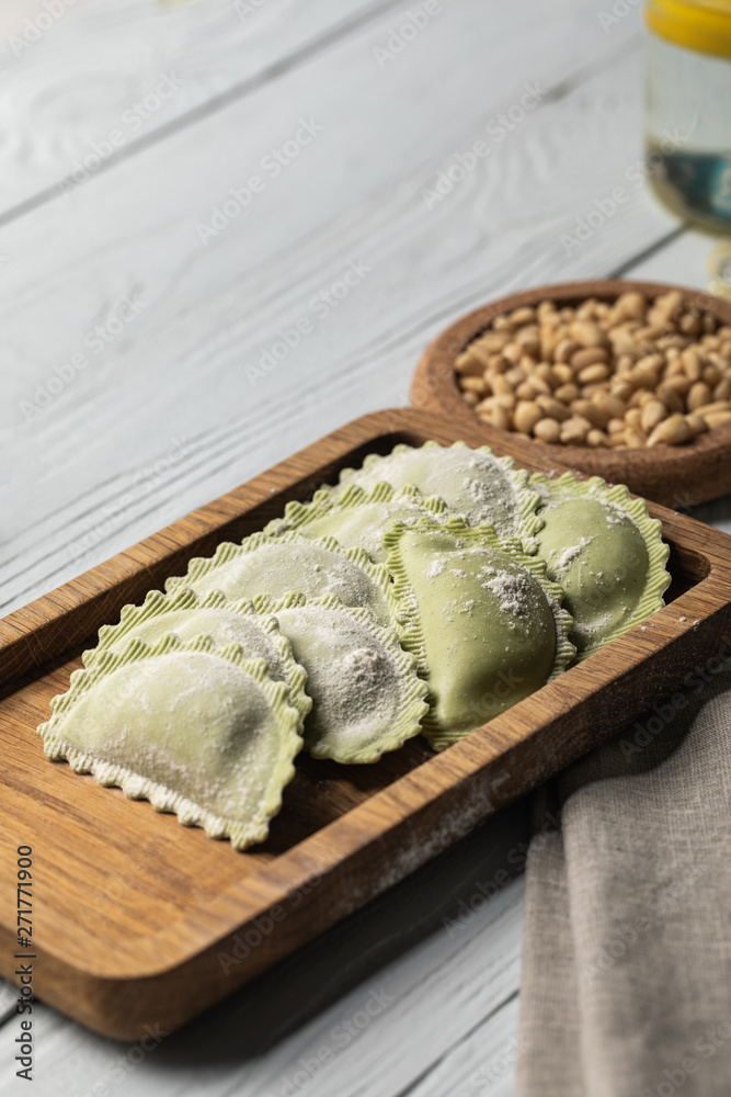 close up view of raw green ravioli with flour on wooden board near pine nuts close up view of raw green ravioli with flour on wooden board near pine nuts