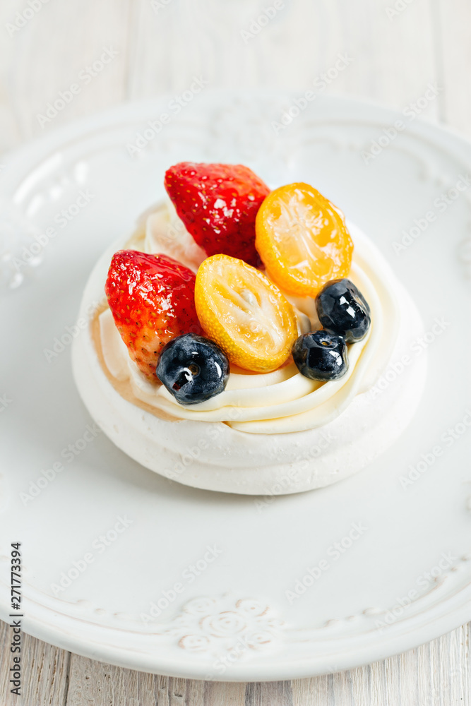 Pavlova's meringue cake with cream and glazed fruit on white plate on wooden table Pavlova's meringue cake with cream and glazed fruit on white plate on wooden table
