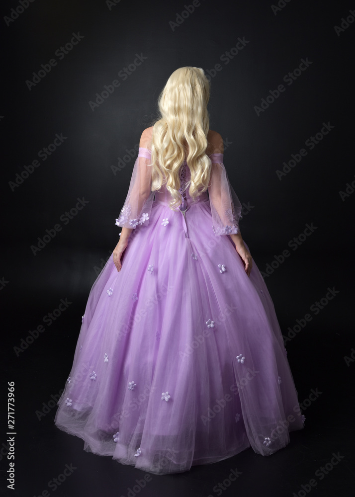 full length portrait of a blonde girl wearing a fantasy fairy inspired costume, long purple ball gown with fairy wings, standing pose on a dark studio background. full length portrait of a blonde girl wearing a fantasy fairy inspired costume, long purple ball gown with fairy wings, standing pose on a dark studio background.