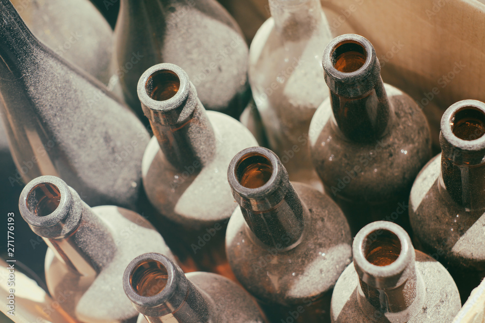 Old empty dusty wine bottles in a box. Brown and clear glass.