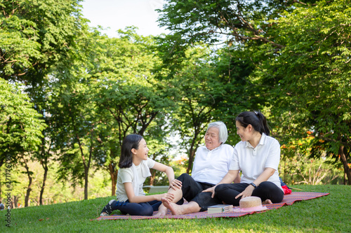 Fototapeta Naklejka Na Ścianę i Meble -  Happy smiling family sitting on mat in outdoor park,asian senior grandmother receiving massage by granddaughter,relax and have fun talking in garden,summer and vacation concept