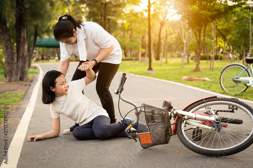 Asian little girl sitting down on the road with a leg pain due to a bicycle accident,bike fall near child,cute girl falling a bicycle ,mother helping,support care of her daughter,accident concept
