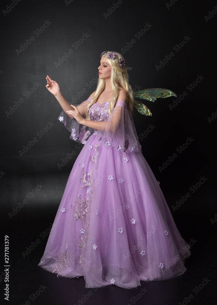 full length portrait of a blonde girl wearing a fantasy fairy inspired  costume, long purple ball gown with fairy wings, standing pose on a dark  studio background. Stock-foto | Adobe Stock