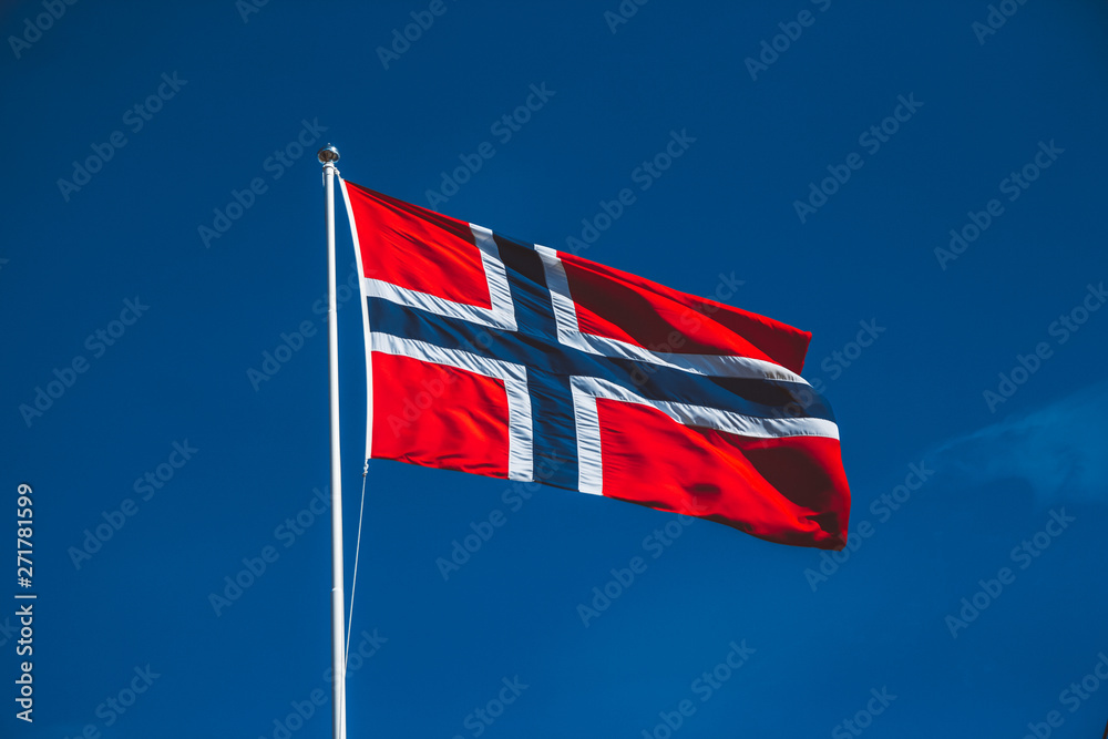 Norwegian flag against the blue sky. The wind blows against the blue sky without clouds - obrazy, fototapety, plakaty 