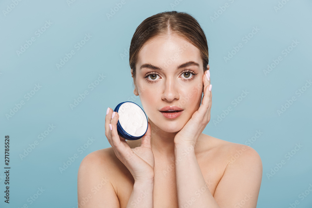 Amazing young woman posing isolated over blue wall background take care of her skin with cream. Amazing young woman posing isolated over blue wall background take care of her skin with cream.