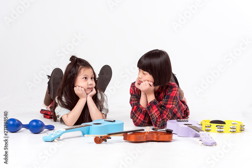 Two cute girls,older sister and younger sister,brethren lay down on the floor in music class,many instrument music in front : blue maracas,purple and blue ukulele,wooden brown violin. photo