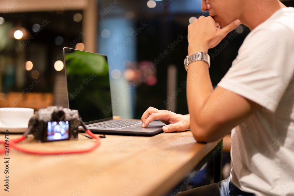 Male working on laptop at night in coffee shop with camera on table. Male working on laptop at night in coffee shop with camera on table.