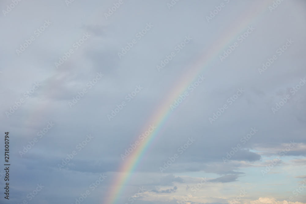rainbow on blue sky background with clouds and sunlight
