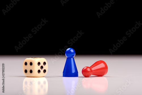 Standing blue playing figurine as winner and lying red figurine as loser with playing dice on white table top with black background - Space for your text.