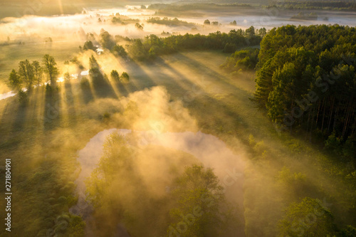 Beautiful summer landscape aerial view. Sun shines through mist on river meadow. Scenic sunny morning on riverside. Summer background with sunbeams