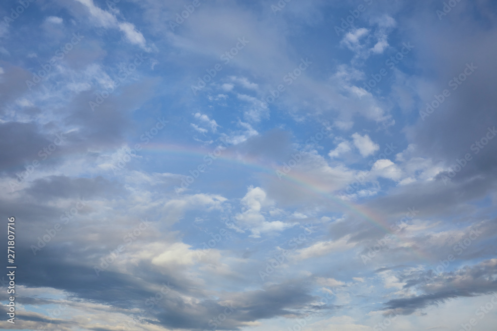 view of rainbow on blue sky background and blue clouds