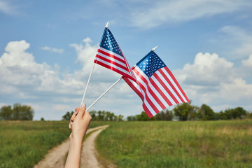 Cropped view of young woman holding american flags in hand on field background