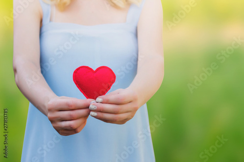 Young woman holding a red heart in her hands against a background of nature. Love, pregnancy, parenthood, motherhood concept, copy space photo