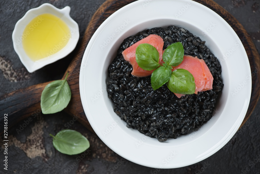 Top view of squid-ink risotto with salmon fillet, green basil and olive oil, studio shot Top view of squid-ink risotto with salmon fillet, green basil and olive oil, studio shot