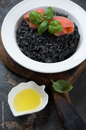Risotto with squid-ink, salmon fillet and fresh green basil in a white plate, close-up, vertical shot