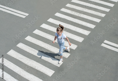 In the summer on the street at the pedestrian crossing kid girl in fashion clothes cross the road. From top view. Shadow at zebra crossing