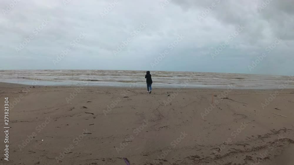 young woman going near sea on the beach. Cheerful girl under the rain during a storm young woman going near sea on the beach. Cheerful girl under the rain during a storm
