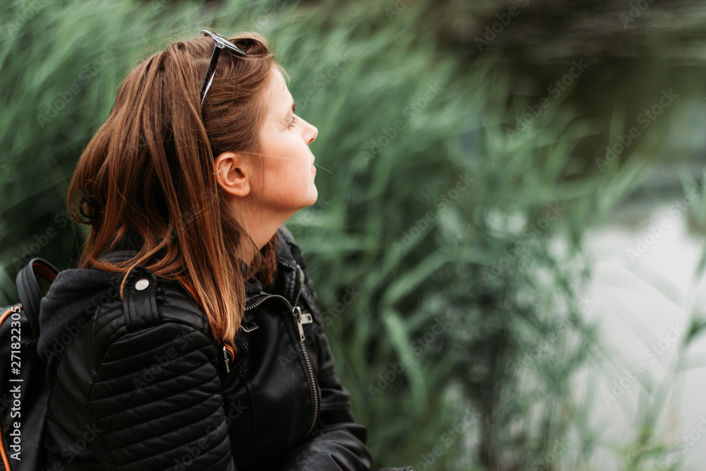 Young woman with short brown hair daydreaming while sitting near a lake in a park – Pretty girl wearing a leather jacket enjoying peaceful moments in a natural environment Young woman with short brown hair daydreaming while sitting near a lake in a park – Pretty girl wearing a leather jacket enjoying peaceful moments in a natural environment