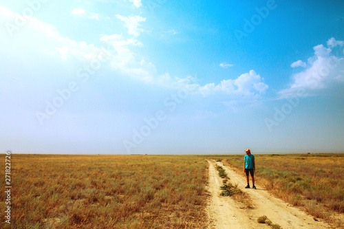 young man standing on the road in savannah. Heat, sun, blue sky. dry ground