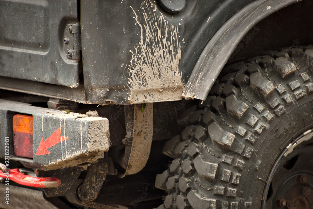 Wheels, lights and bumper are laced in a swamp. Dirty parts of a truck close up.