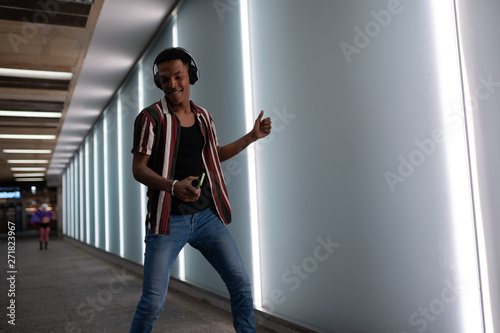 attractive young handsome guy walks in the neon light of the night city listens to music in wireless headphones from a mobile phone and dances fun