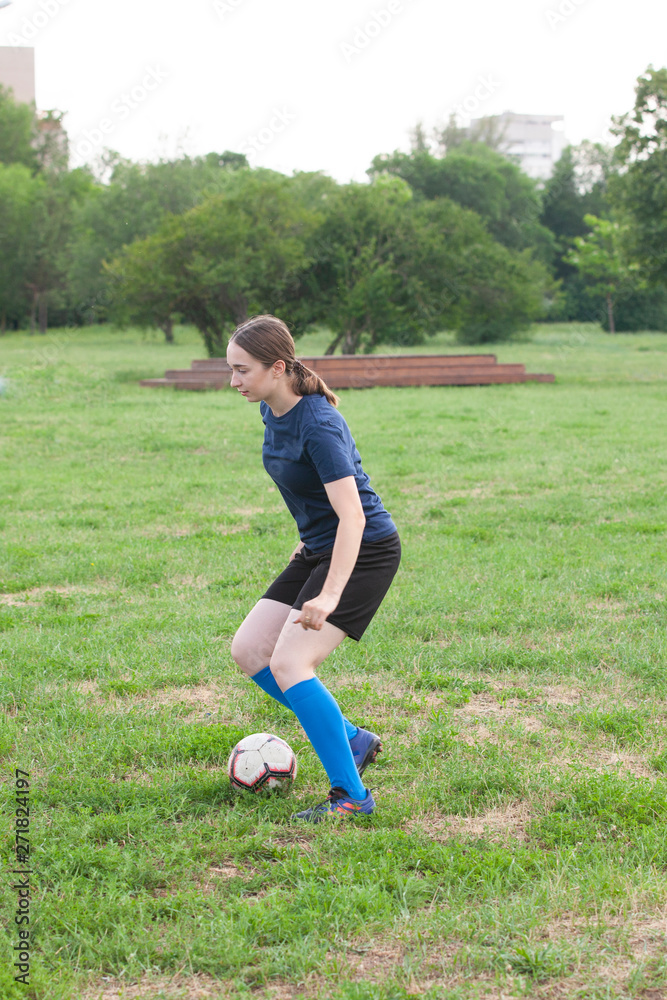 Young female soccer or football player with long hair in sportwear and boots kicking ball for the goal in jump at the stadium. Young female soccer or football player with long hair in sportwear and boots kicking ball for the goal in jump at the stadium.