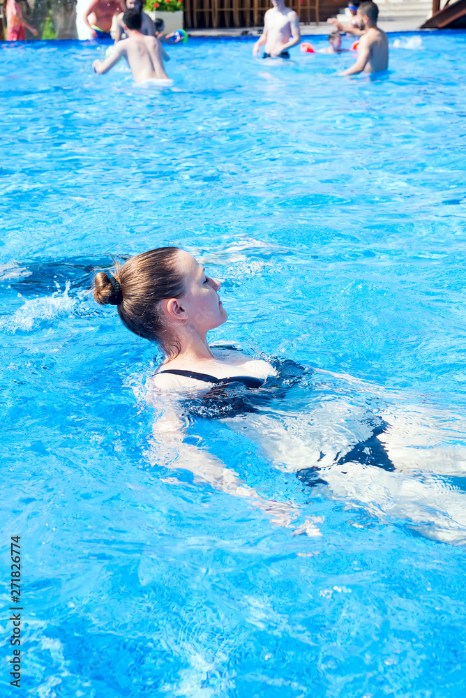 woman with black swimsuit swimming on a blue water pool, tropical vacation holiday concept