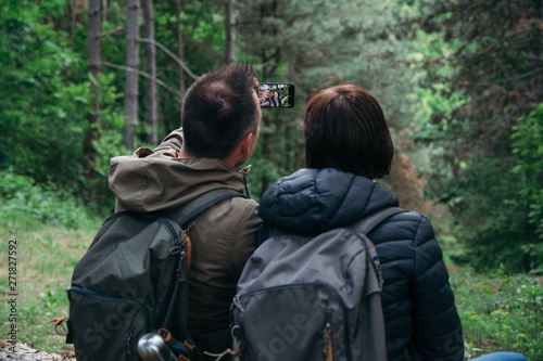 Young couple using smart phone in the forest. Taking picture